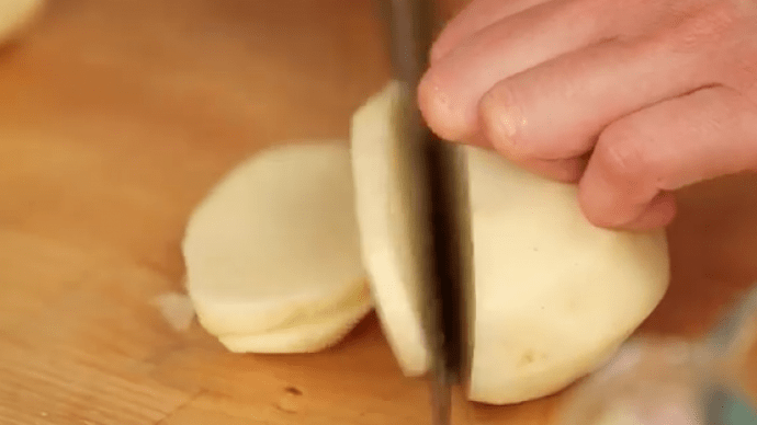Im ersten Schnitt schneidest du die geschälten Kartoffeln in 3 Millimeter dicke Scheiben.